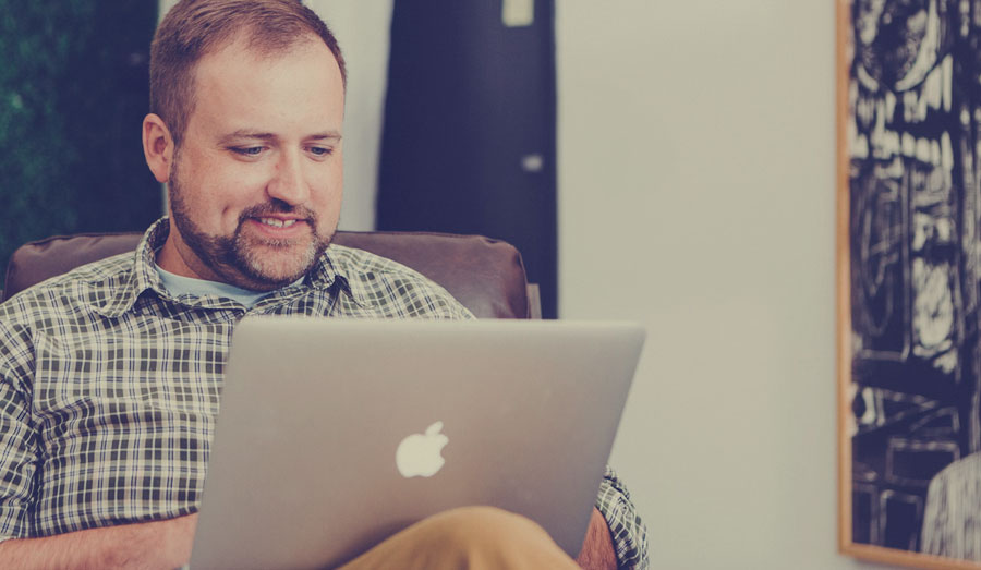 a happy man in a plaid shirt using a laptop