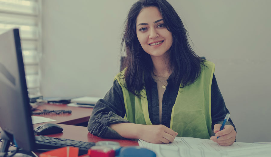 a smiling woman in a neon vest sitting at a cluttered desk